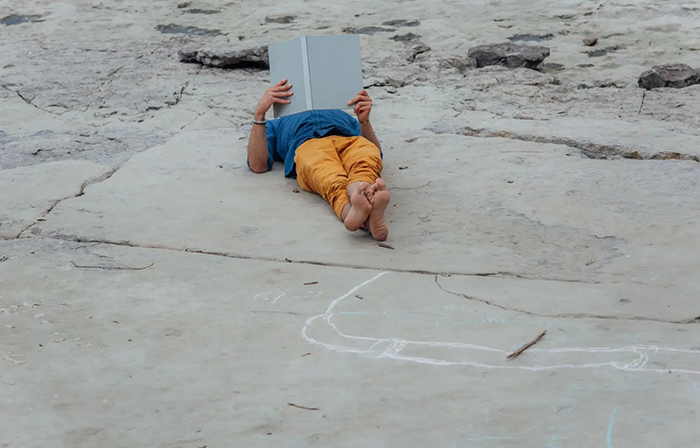 Photo d'un homme couché sur un sol de béton lisant un livre.