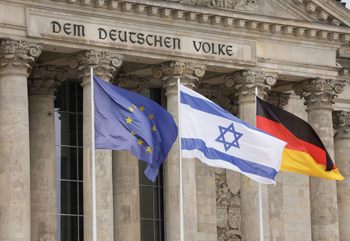 Photo du drapeau d'Israël flottant entre celui de l'Union européenne et celui de l'Allemagne devant le bâtiment du Reichstag à Berlin.