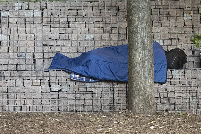 Photo d'une personne dormant sur un banc dans un sac de couchage.