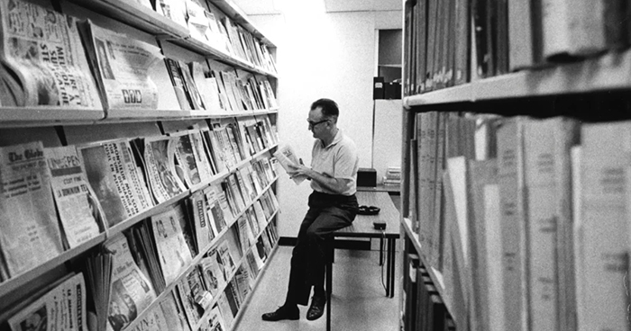 Photo de Pierre Vadeboncoeur lisant un périodique dans une bibliothèque.