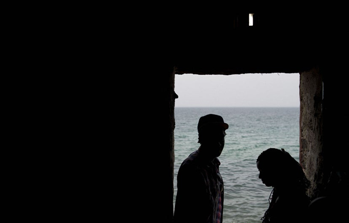 Photo de la silhouette de deux personnes noires que l'on voit à travers une porte donnant sur la mer.