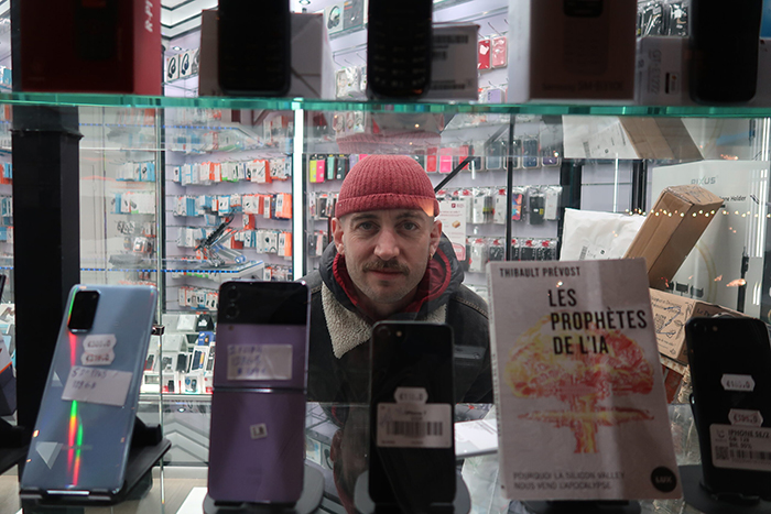 Photo de Thibaut Prévost derrière une vitrine où l'on vend des téléphones et un exemplaire de son livre.