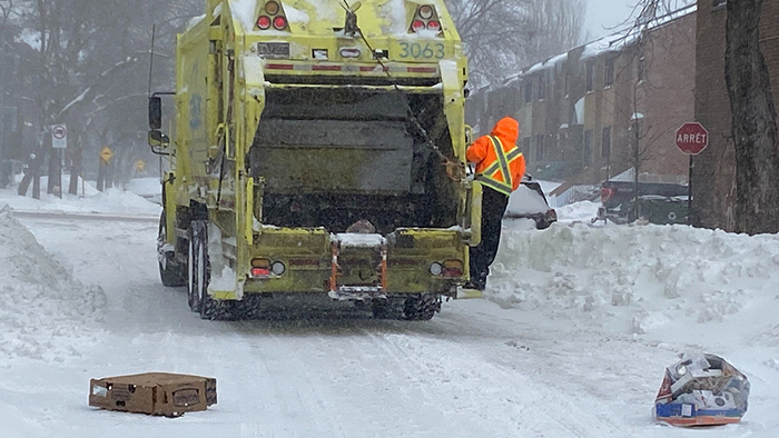 Photo d'un camion de poubelles avançant tant bien que mal dans une rue enneigée.