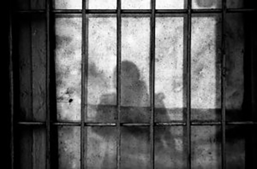 Image de barreaux d'une geôle avec l'ombre d'une personne au mur.