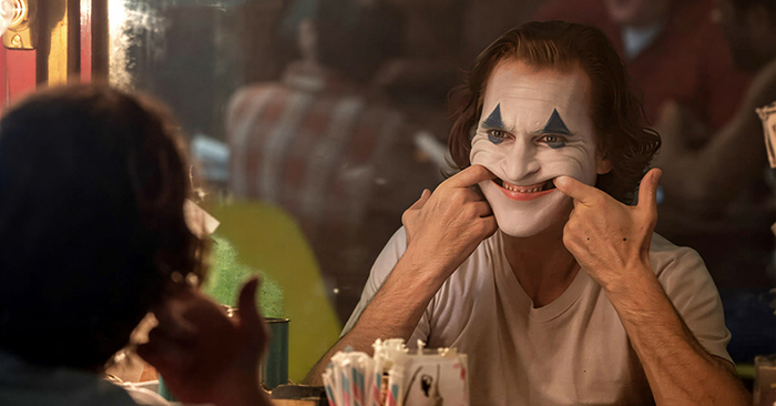 Image tirée du film «Le Joker». Le persopnnage éponyme, devant un miroir, force un sourire en utilisant ses doigts.
