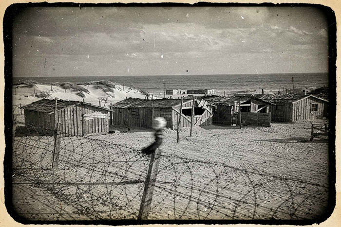 Photo de baraques en bois sur une plage de l'ouest de la France. Le campement est entouré de barbelés.