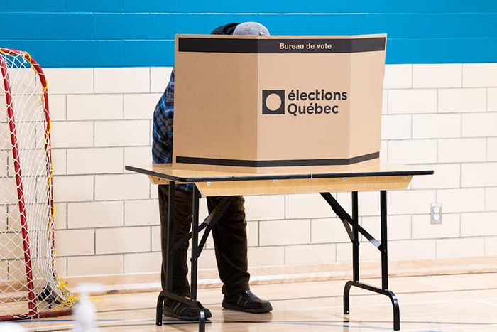 Photo d'un électeur derrière un pupitre, caché par un carton sur lequel il est écrit «Bureau de vote. Élections QUébec».